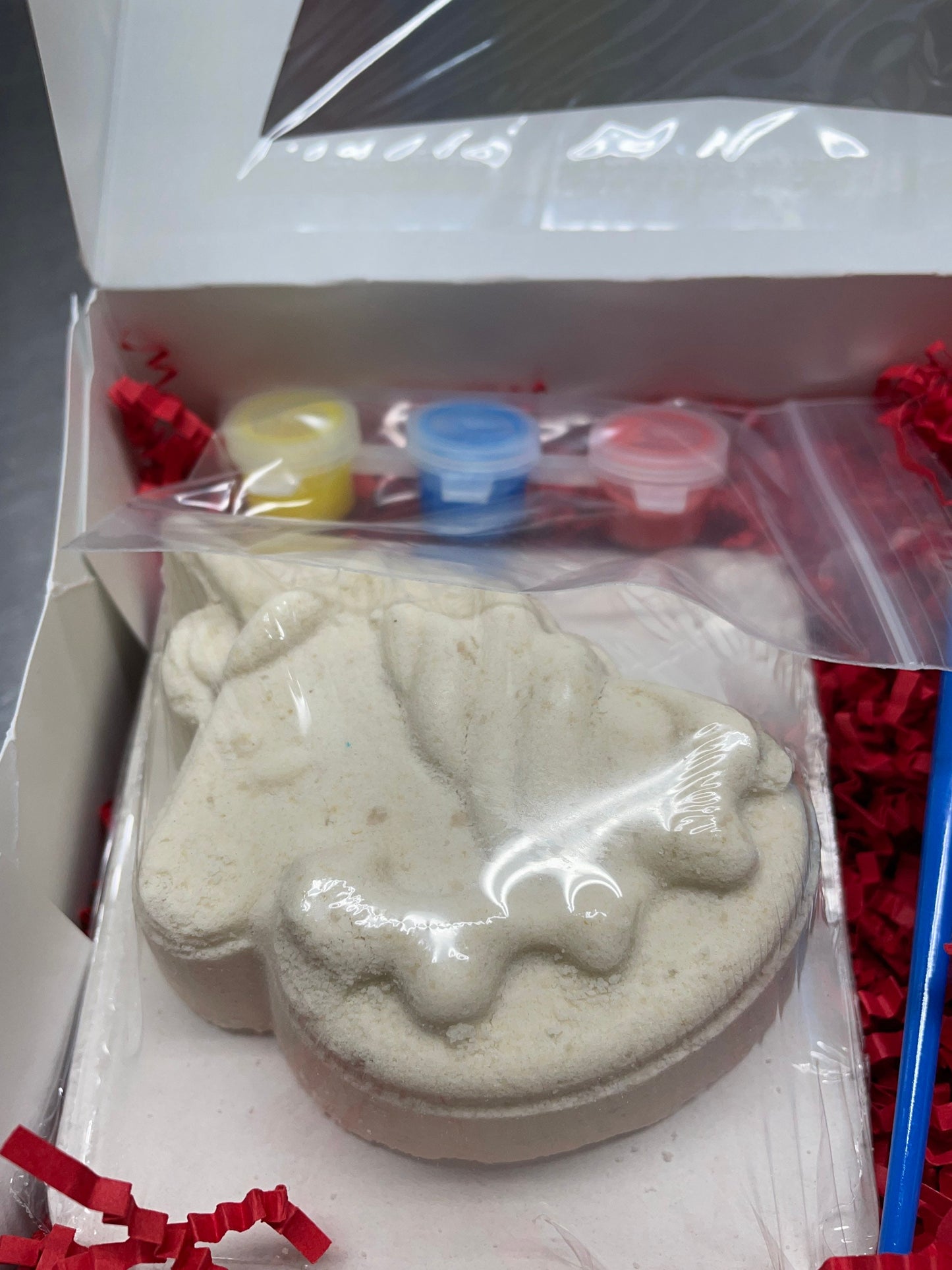 A photo of a box with red bedding with a kit to paint your own bath bomb.