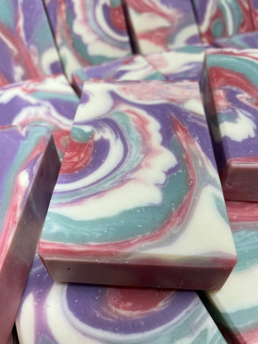 A photo of Love Spell Soap with a swirl of sea moss color, lavender color, creamy color, and red color